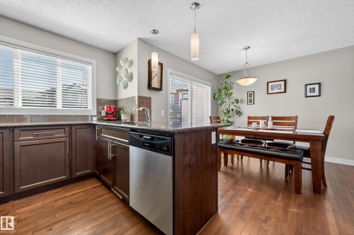 Kitchen featuring wood-finish flooring, dark wood cabinetry, and a stainless steel dishwasher - 1786 Cunningham Way Sw, Edmonton, AB - Indoor