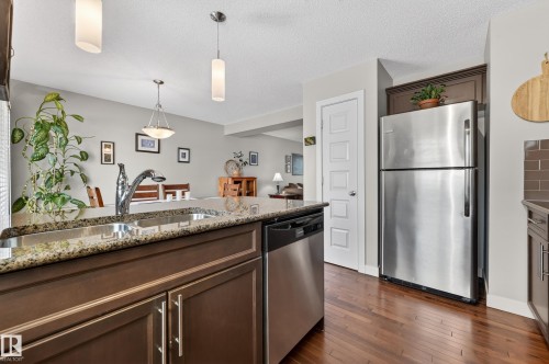 Kitchen featuring a stainless steel undermount sink, granite countertops, dark wood-finish cabinetry, and wood-finish flooring - 1786 Cunningham Way Sw, Edmonton, AB - Indoor Photo Showing Kitchen With Double Sink With Upgraded Kitchen