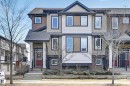 Multi-level townhouse exterior featuring a prominent red entry door with sidelights and transom window, a stone veneer facade, and white trim accents - 1786 Cunningham Way Sw, Edmonton, AB  - Outdoor With Facade 