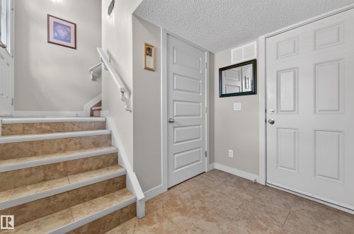 Foyer with light-toned tile flooring, white six-panel entry door, and white five-panel interior door - 1786 Cunningham Way Sw, Edmonton, AB - Indoor Photo Showing Other Room