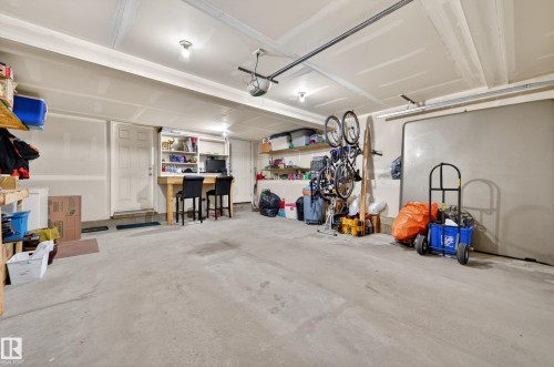 Spacious garage featuring a concrete floor, built-in wooden bar with storage, overhead lighting, and white walls - 1786 Cunningham Way Sw, Edmonton, AB - Indoor Photo Showing Garage