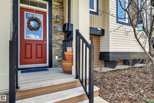 Entryway featuring a red paneled door with a glass insert, stone veneer siding, and contrasting light-toned horizontal siding - 1786 Cunningham Way Sw, Edmonton, AB - Outdoor With Exterior