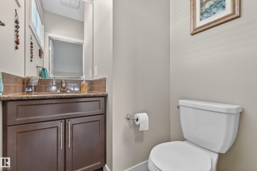 Bathroom vanity featuring a dark wood-finish cabinet with silver-tone pulls, a speckled countertop, and a tiled backsplash - 1786 Cunningham Way Sw, Edmonton, AB - Indoor Photo Showing Bathroom
