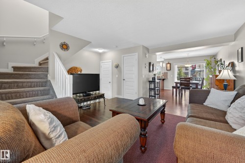 Open-concept living area featuring a carpeted staircase with white railings, dark wood-finish flooring, and white paneled doors - 1786 Cunningham Way Sw, Edmonton, AB - Indoor Photo Showing Living Room