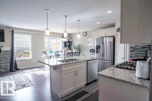 Kitchen featuring an island with double sinks, stainless steel appliances, white cabinetry, granite countertops, and wood-finish flooring - 16619 14 Avenue, Edmonton, AB - Indoor Photo Showing Kitchen With Stainless Steel Kitchen With Double Sink With Upgraded Kitchen
