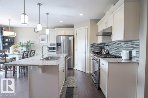 Kitchen featuring light-toned cabinetry, stainless steel appliances, a multi-tone tile backsplash, and a granite island with an undermount sink - 16619 14 Avenue, Edmonton, AB - Indoor Photo Showing Kitchen With Stainless Steel Kitchen With Double Sink With Upgraded Kitchen