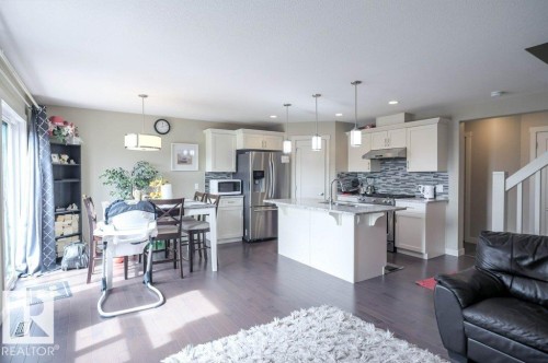 Open-concept living area featuring dark wood-finish flooring, a contemporary kitchen with white cabinetry, stainless steel appliances, and a central island with an undermount sink - 16619 14 Avenue, Edmonton, AB - Indoor Photo Showing Kitchen With Stainless Steel Kitchen With Upgraded Kitchen