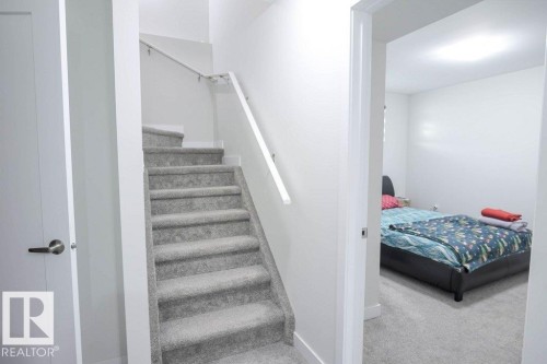 Carpeted staircase with white handrail, contrasting with a white painted wall and a white interior door with brushed nickel hardware - 16619 14 Avenue, Edmonton, AB - Indoor