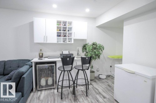Compact wet bar featuring white cabinetry, integrated wine storage, and a stainless steel sink - 16619 14 Avenue, Edmonton, AB - Indoor