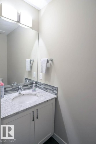 Bathroom vanity with a granite-style countertop, undermount sink, and white cabinetry - 16619 14 Avenue, Edmonton, AB - Indoor Photo Showing Bathroom