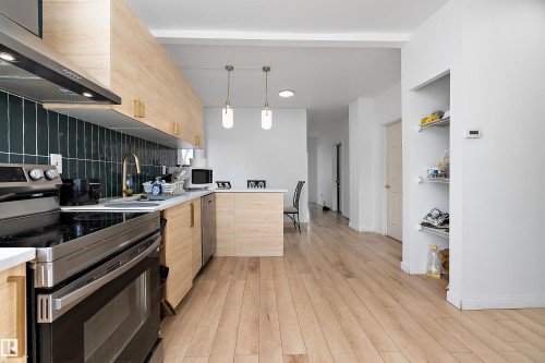 Contemporary kitchen featuring light wood-finish cabinetry, a dark teal subway tile backsplash, and stainless steel appliances - 11919 96 Street, Edmonton, AB - Indoor Photo Showing Kitchen