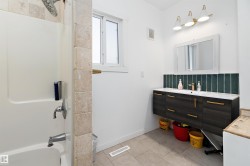 Bathroom featuring a white bathtub, a contrasting dark wood-finish floating vanity with a white countertop, and a tiled backsplash in a vertical pattern - 