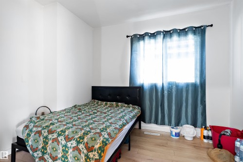 Well-lit room featuring light wood-finish flooring, white walls, and a window with a dark rod and blue curtains - 11919 96 Street, Edmonton, AB - Indoor Photo Showing Bedroom