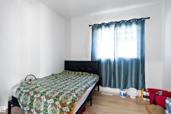 Well-lit room featuring light wood-finish flooring, white walls, and a window with a dark rod and blue curtains - 