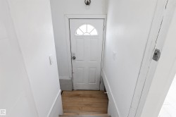 White paneled door with an arched transom window, wood-finish flooring, and white painted walls - 