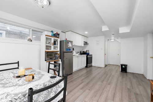 Open-concept kitchen and dining area featuring white cabinetry, stainless steel appliances, and wood-finish flooring - 11919 96 Street, Edmonton, AB - Indoor