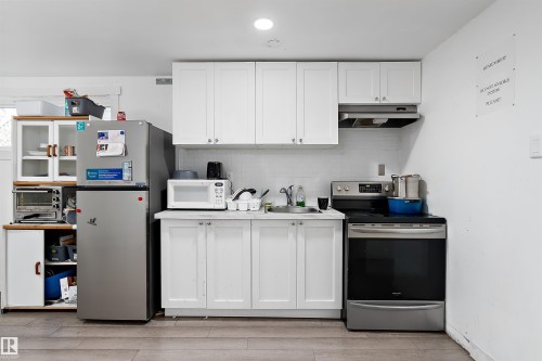 Kitchenette featuring white shaker-style cabinetry, a subway tile backsplash, stainless steel appliances, a single-basin sink, and wood-finish flooring - 11919 96 Street, Edmonton, AB - Indoor Photo Showing Kitchen