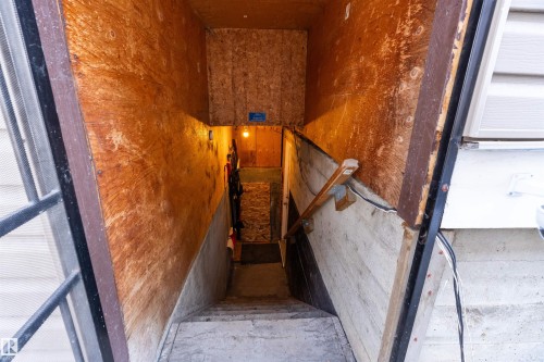 Basement access featuring concrete steps, plywood walls, and a wooden handrail - 11919 96 Street, Edmonton, AB - 