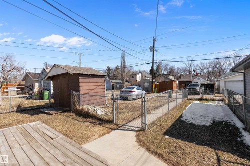Fenced rear yard featuring a concrete pathway, a wooden storage shed, a chain-link fence, and a wooden deck area - 11919 96 Street, Edmonton, AB - Outdoor