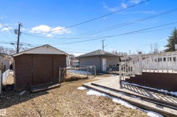 Wooden deck with white railing, brown shed, detached garage with gray siding, and chain-link fencing - 