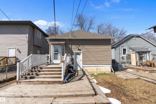 Rear exterior featuring a spacious wood deck with white railings, tan horizontal siding, and a white storm door entryway - 11919 96 Street, Edmonton, AB - Outdoor With Exterior