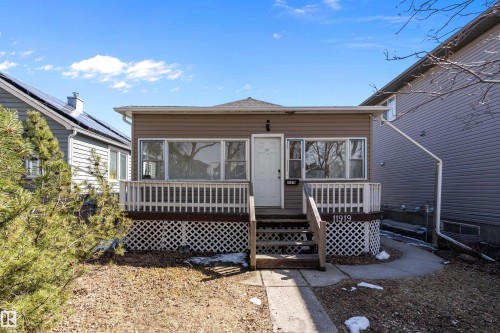 Front façade featuring brown siding, multiple windows, a white entry door, and a front porch with white railings and lattice skirting - 11919 96 Street, Edmonton, AB - Outdoor With Deck Patio Veranda