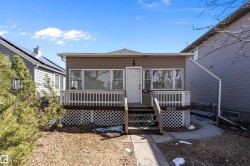 Front façade featuring brown siding, multiple windows, a white entry door, and a front porch with white railings and lattice skirting - 