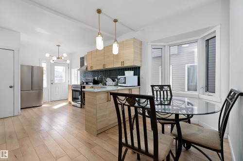 Open-concept kitchen featuring light wood-finish cabinetry, a large bay window, stainless steel appliances, a white countertop island, and pendant lighting - 11919 96 Street, Edmonton, AB - Indoor