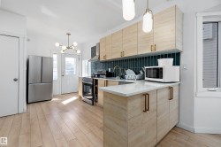 Kitchen with wood-finish flooring, light wood-tone cabinetry, and a dark tile backsplash - 