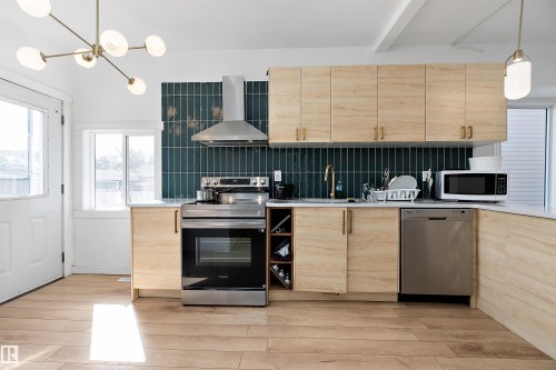 Modern kitchen featuring light wood-finish cabinetry with brass hardware, a deep teal subway tile backsplash, and stainless steel appliances including a range and dishwasher - 11919 96 Street, Edmonton, AB - Indoor Photo Showing Kitchen