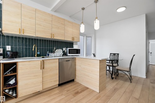 Kitchen featuring light wood-finish cabinetry, a dark teal vertical tile backsplash, stainless steel dishwasher, a gold-finish gooseneck faucet, and light wood-finish flooring - 11919 96 Street, Edmonton, AB - Indoor Photo Showing Kitchen
