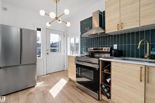 Modern kitchen featuring light wood-finish cabinetry, stainless steel appliances, a dark green vertical tile backsplash, and light wood-finish flooring - 11919 96 Street, Edmonton, AB - Indoor Photo Showing Kitchen