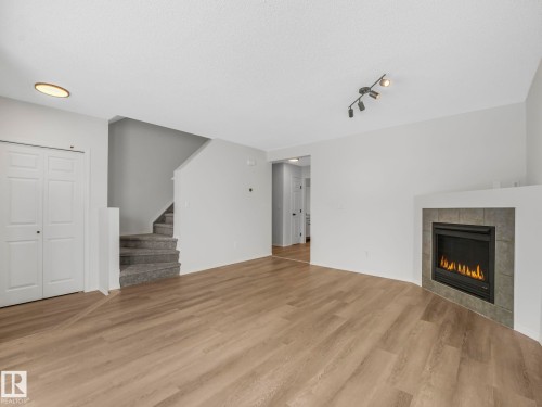The living area features light-colored flooring, a fireplace with a tiled surround, and a ceiling-mounted light fixture - 14 15128 22 Street, Edmonton, AB - Indoor Photo Showing Living Room With Fireplace