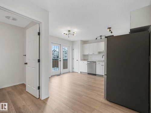 Open concept kitchen and dining area featuring light wood tone flooring, white cabinetry, a black refrigerator, and a stainless steel dishwasher - 14 15128 22 Street, Edmonton, AB - Indoor Photo Showing Kitchen