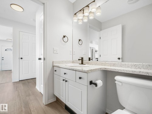 This bathroom features a vanity with a white cabinet and a speckled countertop, complemented by a large mirror and a multi-bulb light fixture - 14 15128 22 Street, Edmonton, AB - Indoor Photo Showing Bathroom