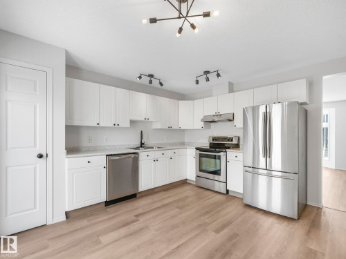 The kitchen features white cabinetry, stainless steel appliances, light-colored countertops, and wood-look flooring - 14 15128 22 Street, Edmonton, AB - Indoor Photo Showing Kitchen