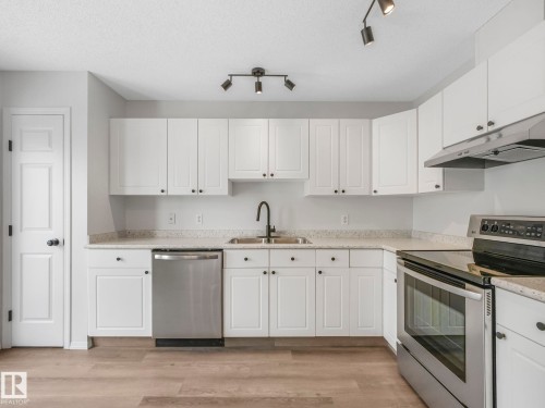 The kitchen features white cabinetry, speckled countertops, and stainless steel appliances including a dishwasher, oven, and range hood - 14 15128 22 Street, Edmonton, AB - Indoor Photo Showing Kitchen With Double Sink