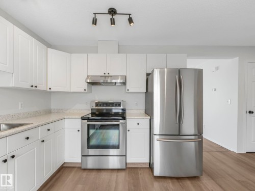 The kitchen features white cabinetry, light-colored countertops, stainless steel appliances including a refrigerator and range, and track lighting - 14 15128 22 Street, Edmonton, AB - Indoor Photo Showing Kitchen