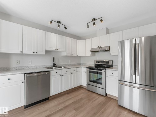 The property features a kitchen with white cabinetry, stainless steel appliances, and light-toned countertops - 14 15128 22 Street, Edmonton, AB - Indoor Photo Showing Kitchen With Double Sink
