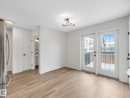 The property features light-toned flooring, a modern ceiling light fixture, and double glass doors leading to an exterior balcony - 14 15128 22 Street, Edmonton, AB - Indoor Photo Showing Other Room