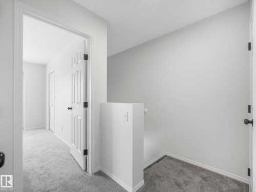 Interior hallway featuring light grey walls, white doors with black hardware, and grey carpet flooring - 14 15128 22 Street, Edmonton, AB - Indoor Photo Showing Other Room