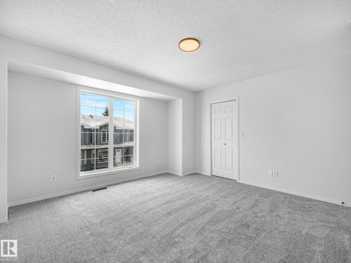 This room features light grey carpeting, white walls, and a large window with white framing - 14 15128 22 Street, Edmonton, AB - Indoor Photo Showing Other Room