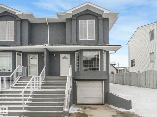 The property features a private garage, exterior stairs with white railings, and bay windows - 14 15128 22 Street, Edmonton, AB - Outdoor With Facade