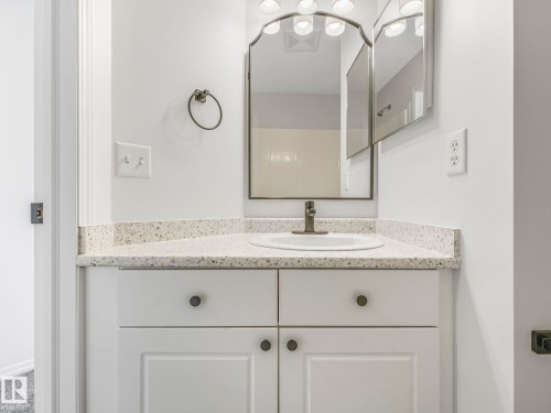 Bathroom vanity featuring a light-colored countertop with an integrated sink, a dark-toned faucet, and a wall-mounted mirror with overhead lighting - 14 15128 22 Street, Edmonton, AB - Indoor Photo Showing Bathroom