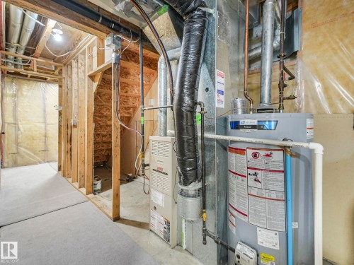 Unfinished basement area featuring a water heater and furnace, exposed wooden studs, and a partial staircase - 14 15128 22 Street, Edmonton, AB - Indoor Photo Showing Basement
