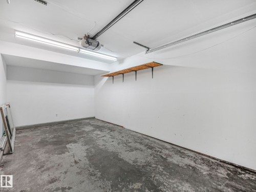 The property features a garage with a concrete floor, white walls, overhead lighting, and built-in shelving - 14 15128 22 Street, Edmonton, AB - Indoor Photo Showing Garage