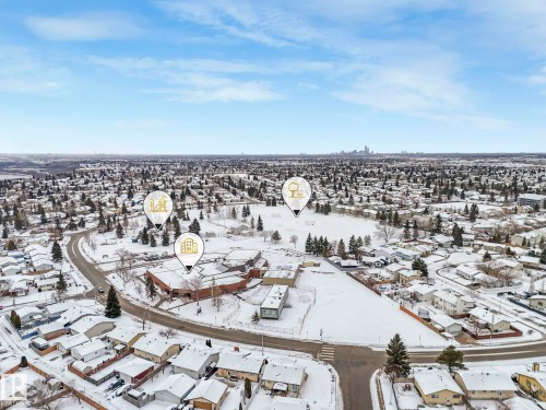 Aerial view showcasing a residential area with snow-covered rooftops and trees, a large open space, and a building with a distinctive red brick exterior - 14 15128 22 Street, Edmonton, AB - Outdoor With View