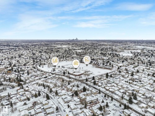 Aerial view showcasing a residential area with snow-covered rooftops and trees, a distant cityscape on the horizon, and a clear sky overhead - 14 15128 22 Street, Edmonton, AB - Outdoor With View