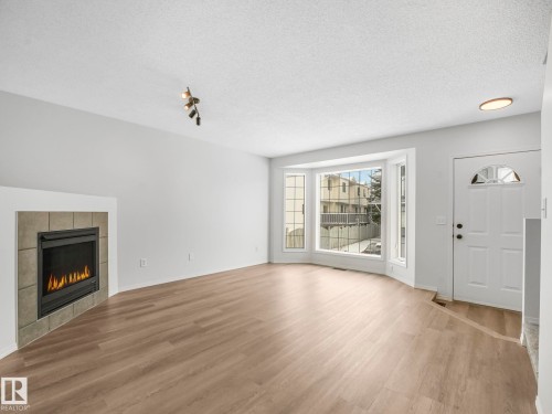 Living area featuring light wood-style flooring, a fireplace with a tiled surround, and a bay window providing natural light - 14 15128 22 Street, Edmonton, AB - Indoor Photo Showing Living Room With Fireplace