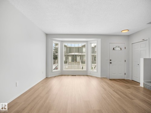 This bright living area features light wood flooring, a bay window with white trim, and a white front door with an arched window insert - 14 15128 22 Street, Edmonton, AB - Indoor Photo Showing Other Room
